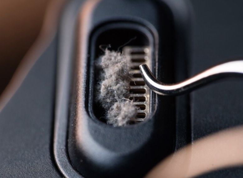 An extreme close-up of a phone charging port densely packed with compacted pocket lint.